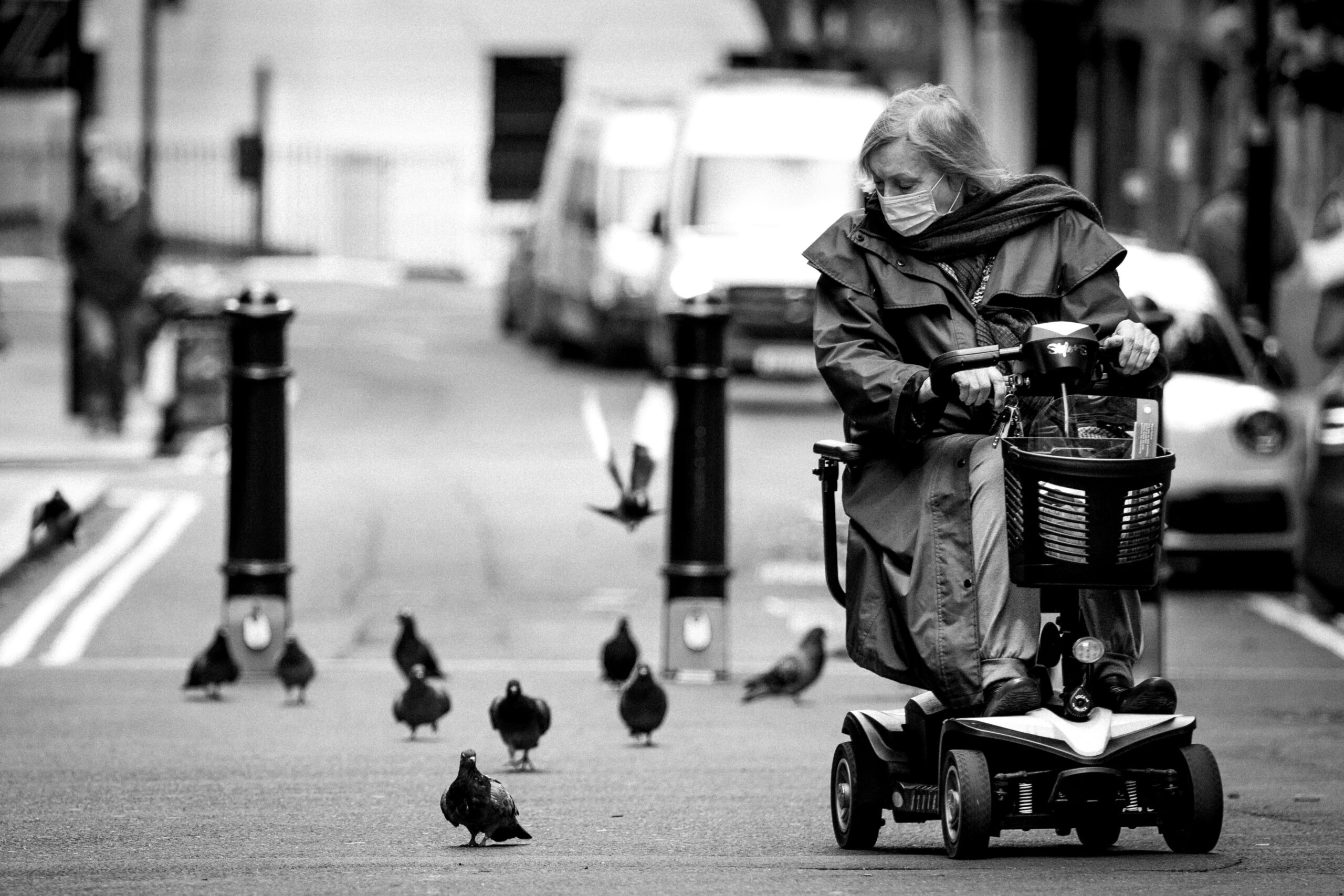 A black and white photo of a woman on a mobility scooter going by some pigeons